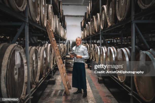 porträt des seniors zwischen fässern im keller. - schnapsbrennerei stock-fotos und bilder