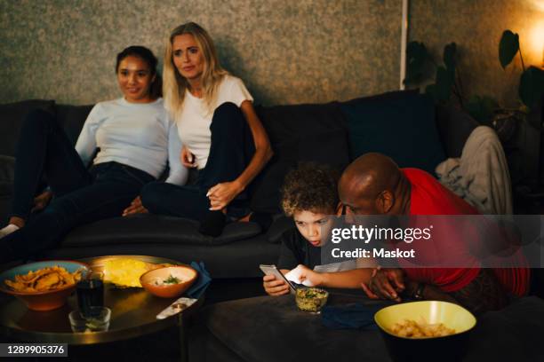 boy using smart phone by father while mother and daughter sitting on sofa during sporting event - mother media call stock pictures, royalty-free photos & images