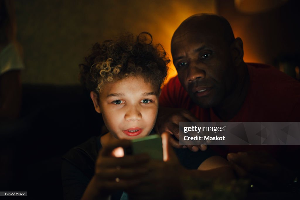Boy using smart phone by father in living room at night