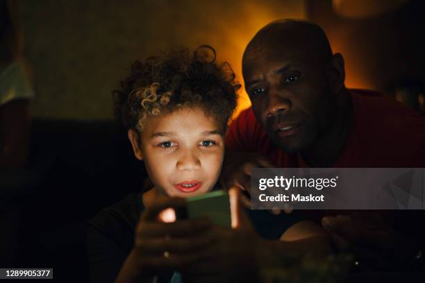 boy using smart phone by father in living room at night - kids watching tv no adult stock pictures, royalty-free photos & images