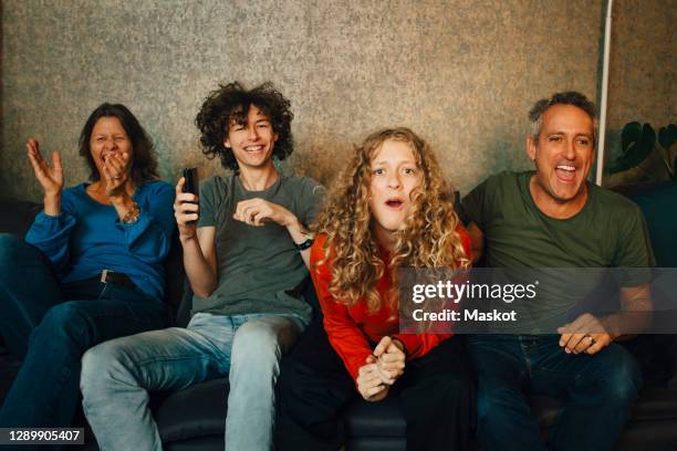 happy parents and children cheering while watching sports in living room at night - familie fernsehen stock-fotos und bilder