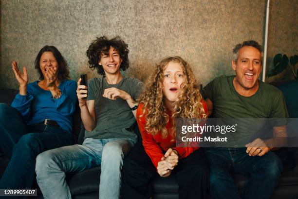happy parents and children cheering while watching sports in living room at night - family watching tv - fotografias e filmes do acervo
