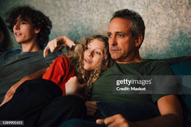 father watching sports with children in living room at night - family on sofa stock-fotos und bilder