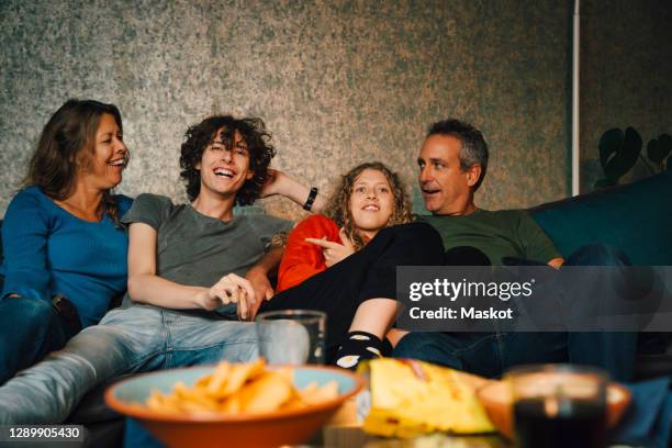 smiling parents with children watching sports in living room at night - family game night stock-fotos und bilder