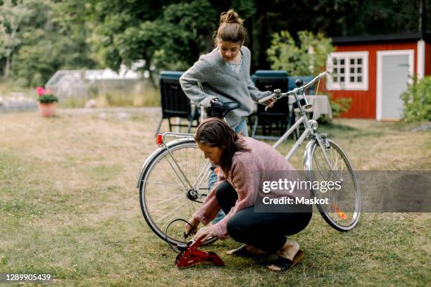 daughter looking at mother pumping bicycle in yard - air pump stock pictures, royalty-free photos & images