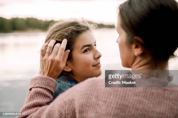 smiling daughter looking at caring mother by lake - season 14 stockfoto's en -beelden