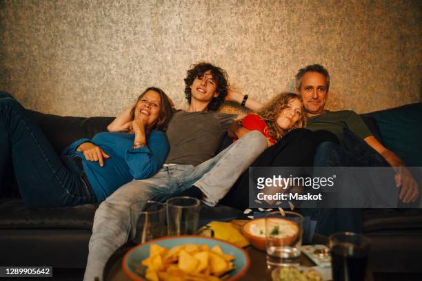 smiling parents and children watching sports in living room at night - family game night stock-fotos und bilder
