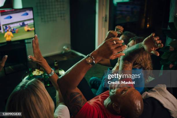 high angle view of friends cheering while watching sports on tv in living room - watching sport television stock pictures, royalty-free photos & images
