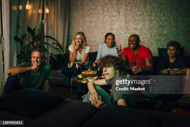 smiling friends and family watching sports at night - boy at television stockfoto's en -beelden