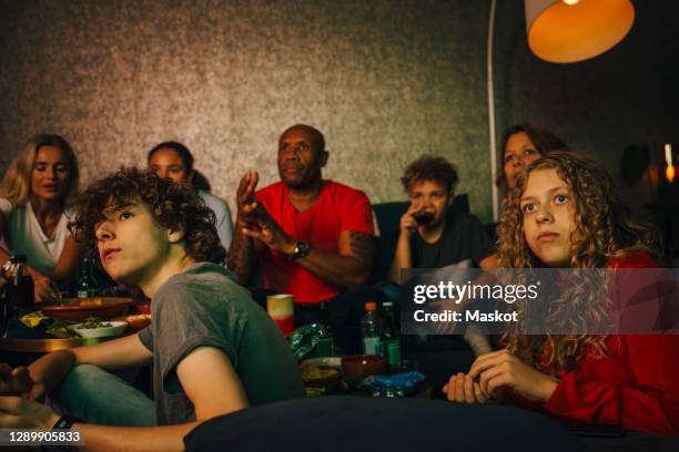 male and female teenagers watching sports with family at night - family watching tv together stock pictures, royalty-free photos & images