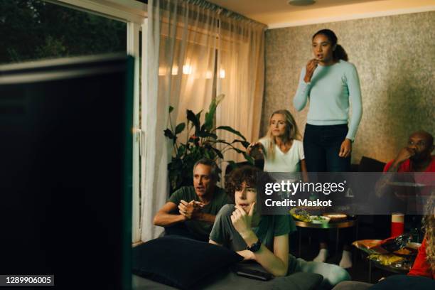 male teenager with family by sofa watching tv during sporting event at night - bald girl stock pictures, royalty-free photos & images
