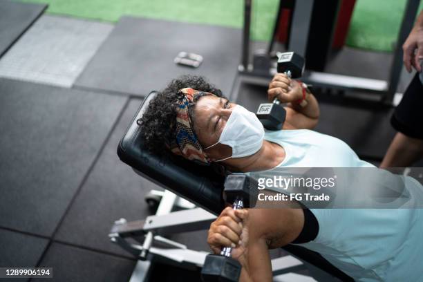 senior in der anwendung von gesichtsmaske mit hantel im fitnessstudio - black female bodybuilder stock-fotos und bilder
