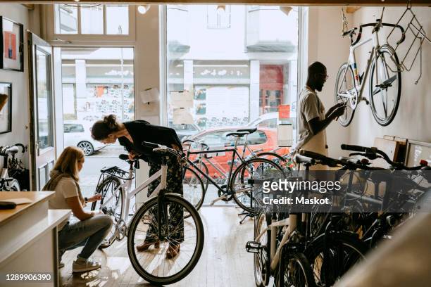 female owner repairing bicycle of senior customer while colleague working on bike at workshop - repair shop bildbanksfoton och bilder