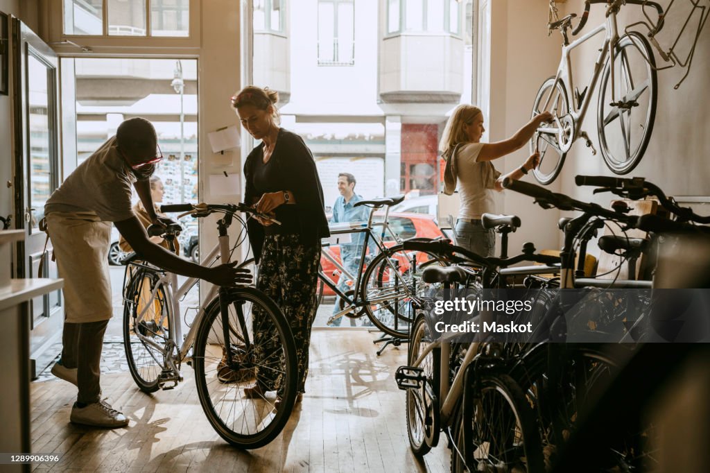 Male owner repairing bicycle of senior customer while colleague working on bike at workshop