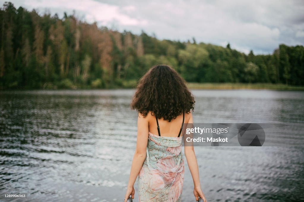 Rear view of teenage girl with curly hair in swimwear walking towards lake during summer