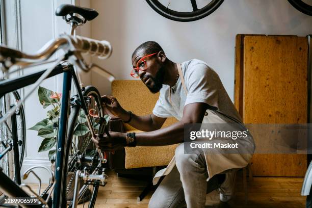 male owner repairing bicycle in workshop - fietsenwinkel stockfoto's en -beelden