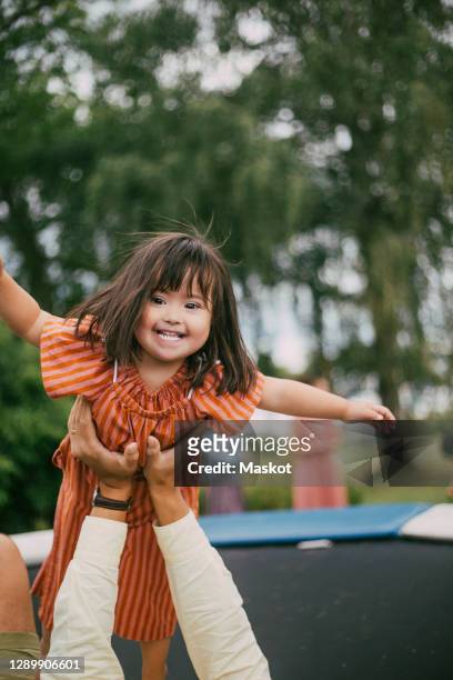 portrait of smiling down syndrome daughter playing with father on trampoline during summer - downsyndrom stock-fotos und bilder