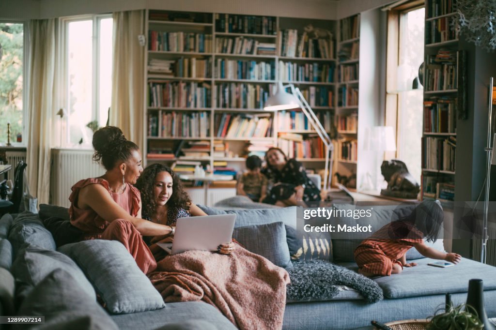 Smiling mother with daughter holding laptop while disabled girl using phone in living room