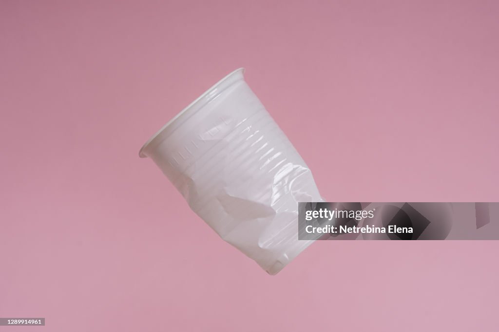 A disposable plastic Cup flies on a pink background. garbage, plastic dishes