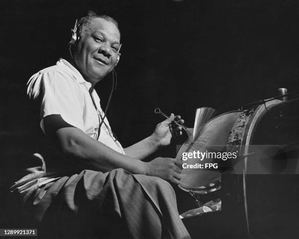 Drummer wearing headphones, possibly during a recording session, turns to look at the camera while keeping the beat with brushes on a snare drum,...