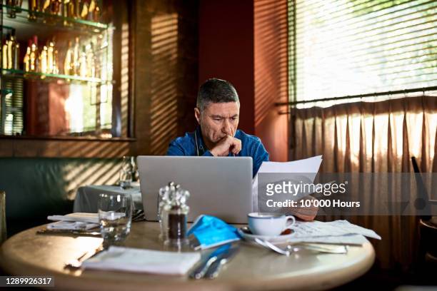 serious looking man reading document in restaurant with face mask on table - cashflow stock-fotos und bilder
