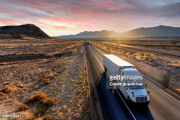 white semi-trailer truck heading down a four-lane highway at dusk - truck stock pictures, royalty-free photos & images