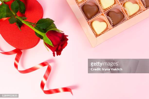 red rose flower with a heart shaped box and chocolate candy for valentine's day over a pastel pink background. - box of chocolate foto e immagini stock