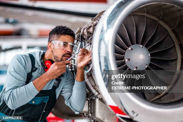 junger männlicher ingenieur, der den flugzeugjet überprüft - flugzeugmechaniker stock-fotos und bilder