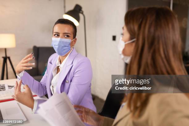 zakenvrouwen met gezichtsmaskers die in bureau spreken - infection prevention stockfoto's en -beelden