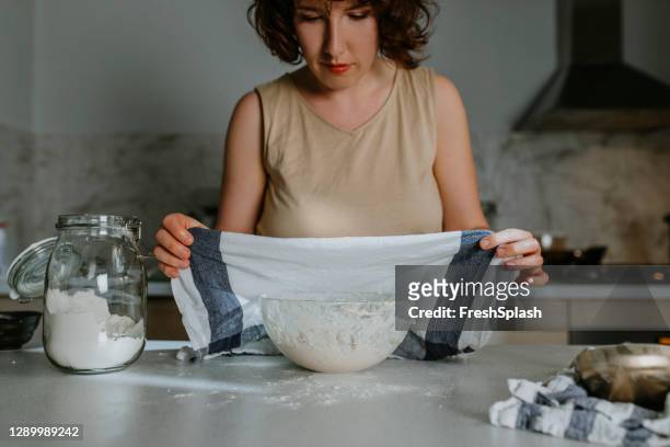 home hobby's: een vrouw bakken zuurdesem brood uit het niets - putting een keukenhanddoek over het deeg om het te laten rusten en bewijs - rijzen stockfoto's en -beelden