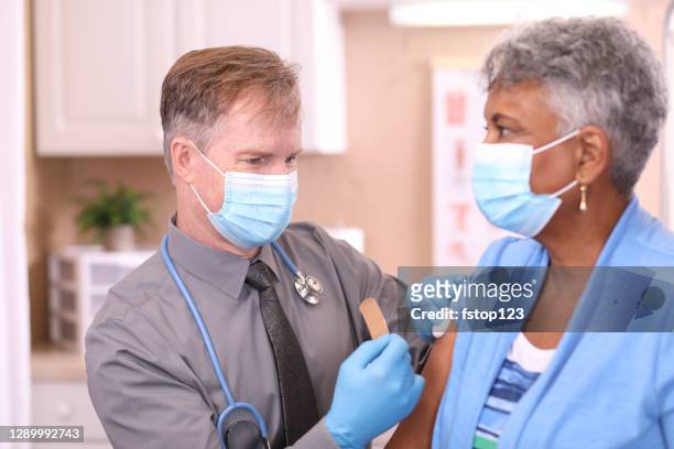 covid-19: doctor and senior adult, african descent patient, vaccine, masks. - african american band aids stock pictures, royalty-free photos & images