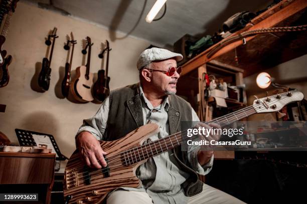 senior man singing and playing on a guitar in instrument maker's workshop - male guitarist stock pictures, royalty-free photos & images
