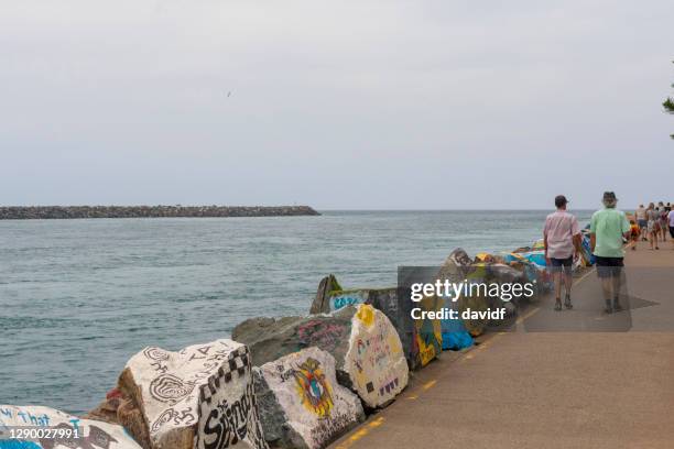 people walking on the break wall at port macquarie alongside murals on the rocks - port macquarie stock pictures, royalty-free photos & images