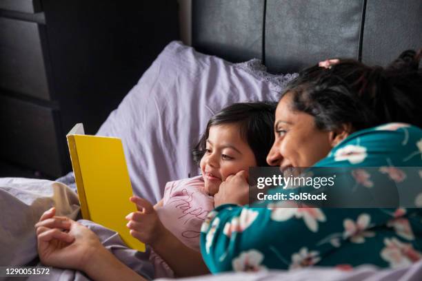 mutter und tochter lesen ein buch im bett - pakistanischer abstammung stock-fotos und bilder