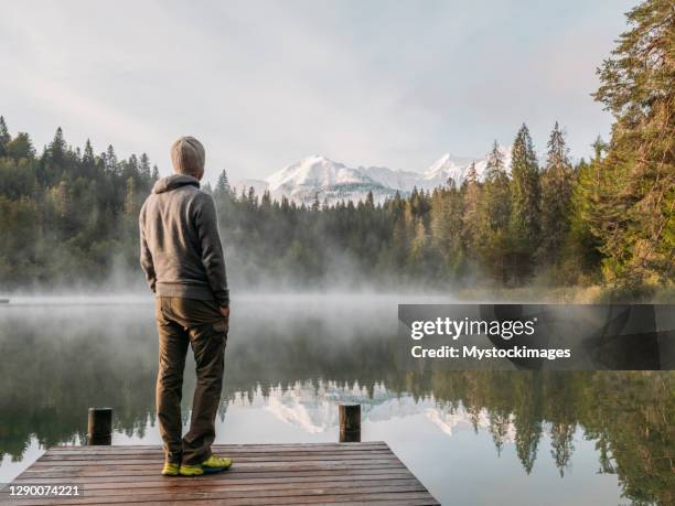 de mens ontspant op houten pijler, kijkt uit over meer - bergsteiger stockfoto's en -beelden