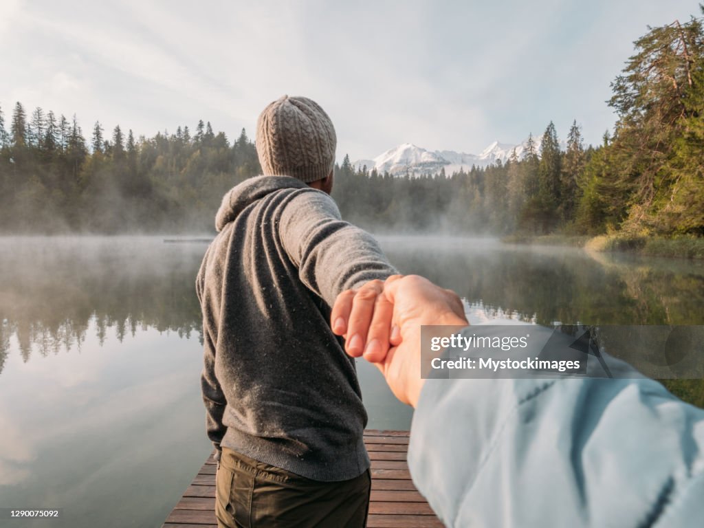 Man leads girlfriend onto wooden dock at sunrise
