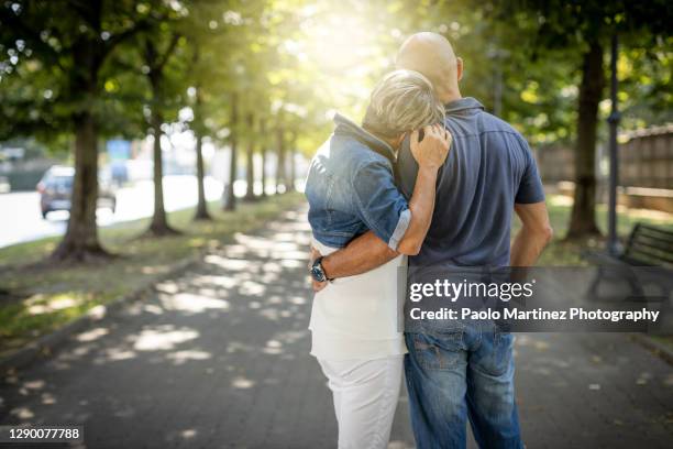 happy mature couple standing in a park, she rests her head on his shoulder - pareja de mediana edad fotografías e imágenes de stock