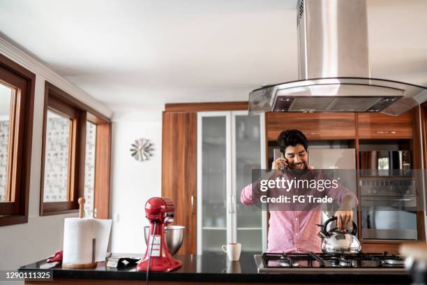 mid adult man boiling water and talking on the phone at home - boiling kettle stock pictures, royalty-free photos & images