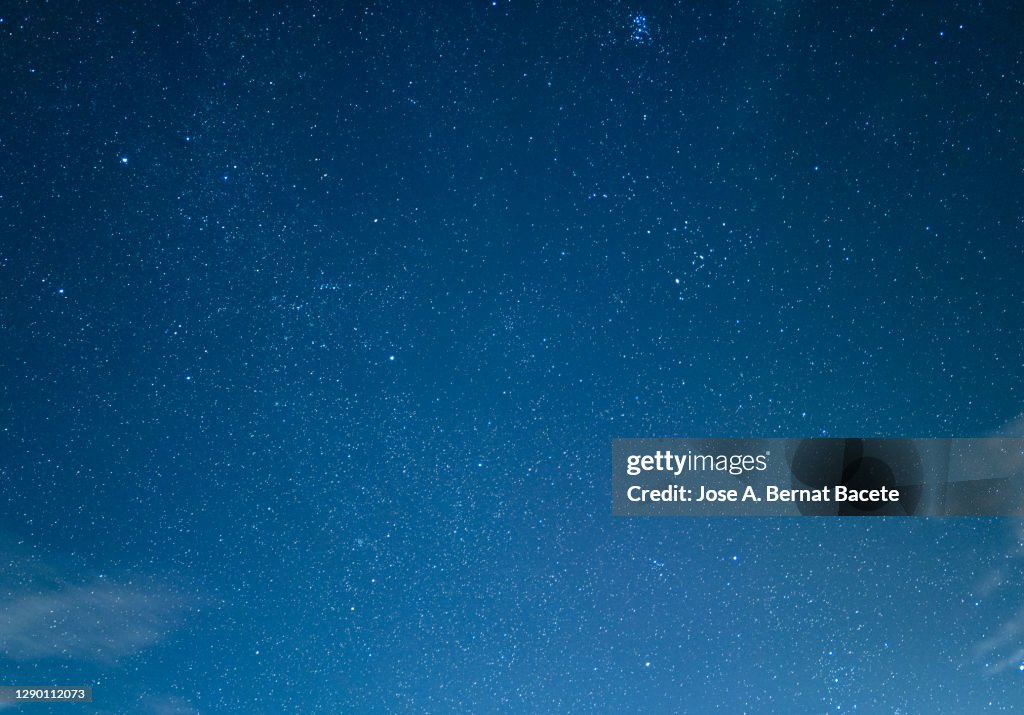 Full frame of blue sky at night with stars and some tall clouds.