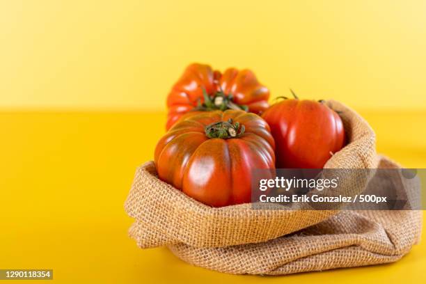 close-up of tomatoes in sack against yellow background - alimentation background stock pictures, royalty-free photos & images