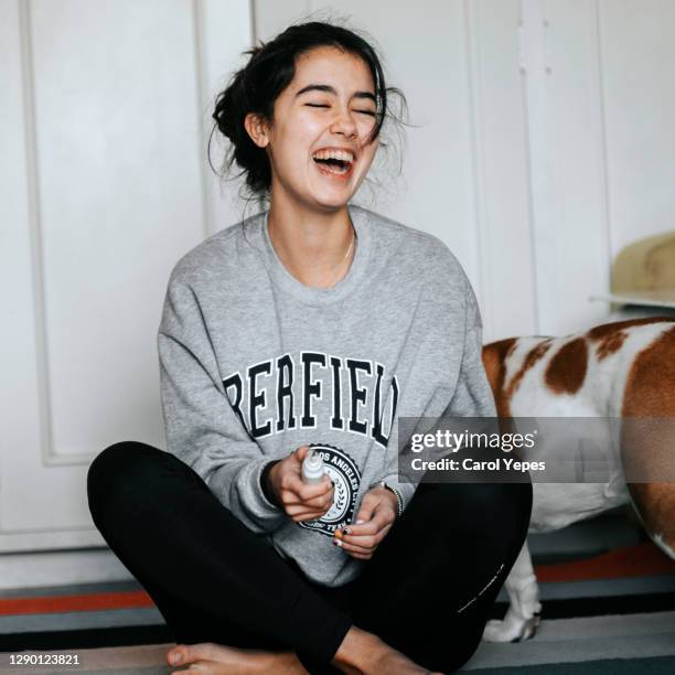 young female in casual clothes having fun sitting on carpet...while dog is sitting close to her - spain teen face stock-fotos und bilder