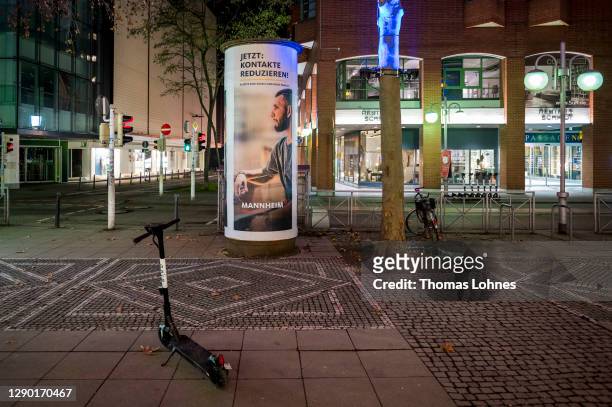 An advertising pillar with the slogan 'Reduce contacts now' stands in an empty pedestrian shopping street during an evening curfew during the second...