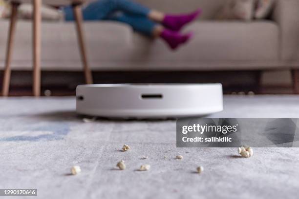 close-up shoot of a woman relaxing and eating popcorns while a robotic vacuum cleaner working - robot vacuum stock pictures, royalty-free photos & images