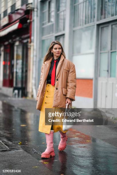 Natalia Verza aka "Mascarada Paris" wears a Prada total look made of a brown winter oversized puffer long Prada coat, a black Prada shirt, a red...