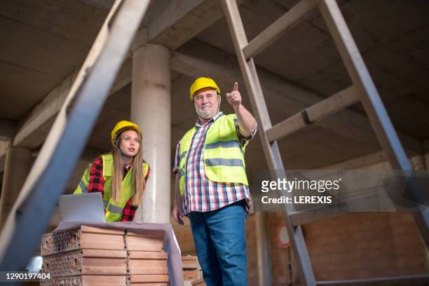 a senior architect trains a young architect on a construction site - foundations conversations with suits stock-fotos und bilder