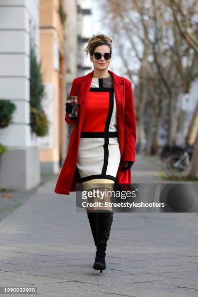 German actress Alexandra Kamp wearing black knee high boots by Salvatore Ferragamo, a red coat by Celvin Klein, sunglasses by Freudenhaus Eyewear,...