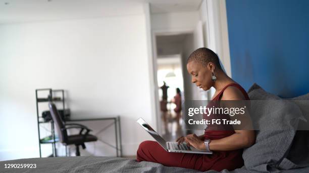 mature woman working from home using laptop in bed - shaved head stock pictures, royalty-free photos & images