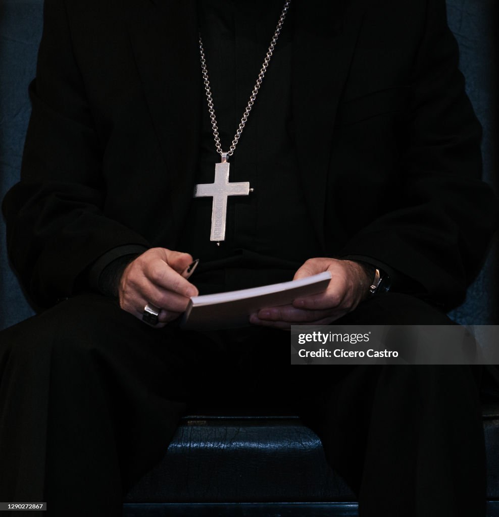 Priest wearing a cross hanging on his chest and holding a book