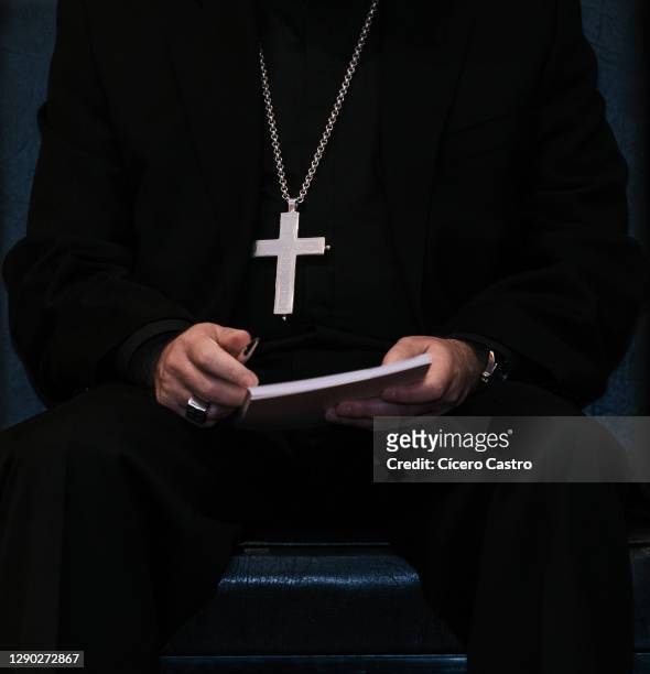priest wearing a cross hanging on his chest and holding a book - collar stock-fotos und bilder