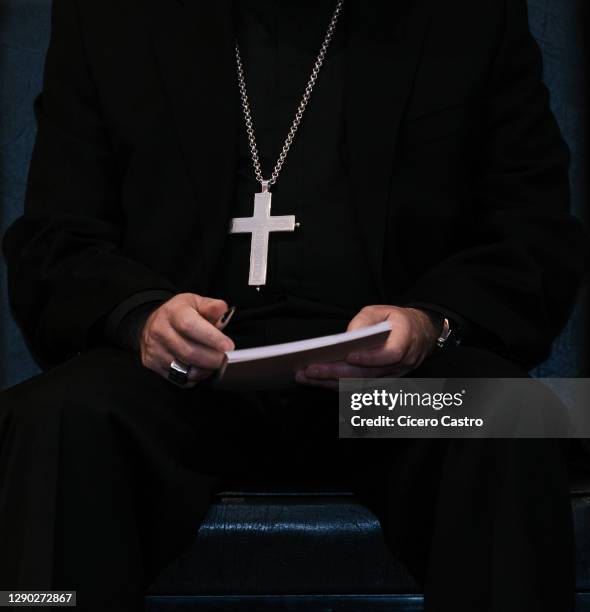 priest wearing a cross hanging on his chest and holding a book - minister foto e immagini stock